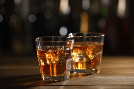 A couple of cocktail glasses filled with dark liquid and ice cubes sit side by side on top of a bar