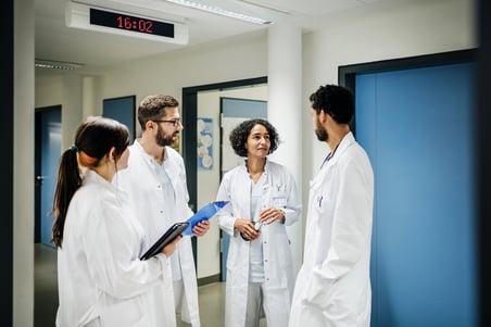 A group of clinical doctors with charts chatting on the ward at the hospital