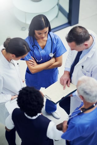 A group of doctors talking together over a medical chart while standing in a hospital