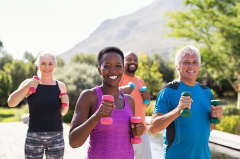 A group of people smile as they run outside together with weights