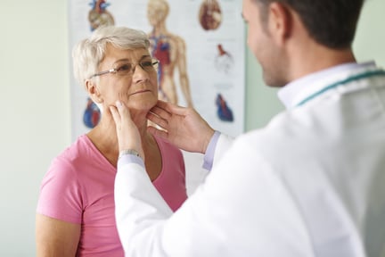 A male healthcare provider uses fingers to examine a female patient’s neck