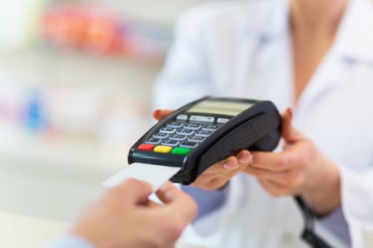 A patient places a credit card into a payment terminal held by a front desk attendant