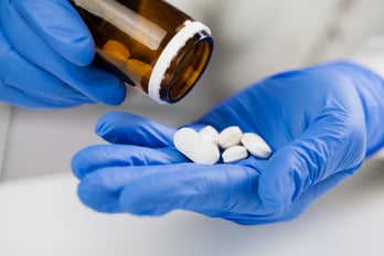 A person with gloved hands pouring pills into his palm