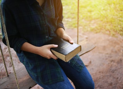 Una mujer sostiene una Biblia sentada en un columpio