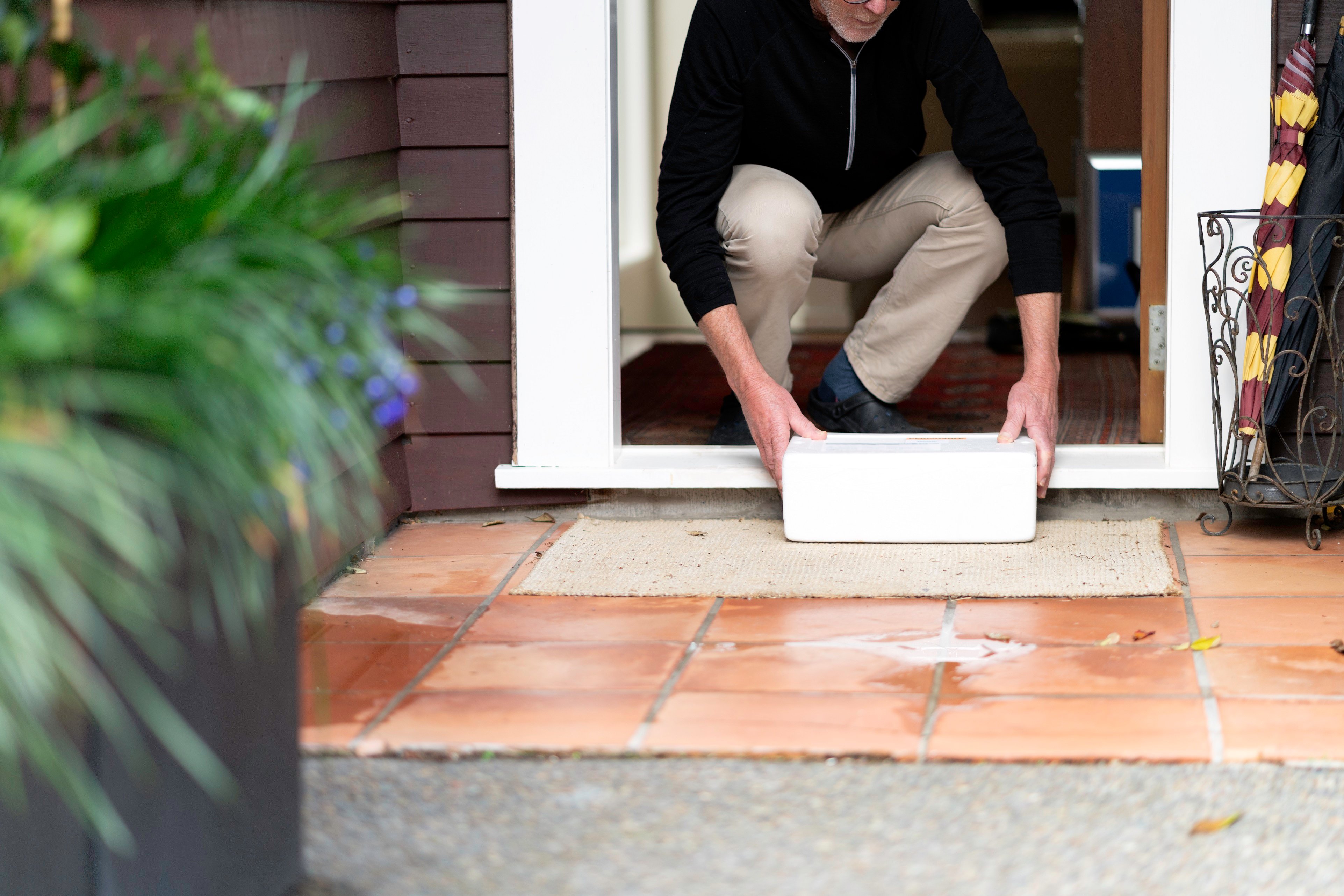 An older man stoops down to pick up a package sitting on his doorstep