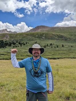 Brandon Martin stands in a field with his right arm in a strong-man pose under a cloudy sky