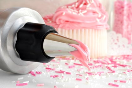 Cake decorating with fresh strawberry frosting dripping from pastry tip and cupcakes with sprinkles in background