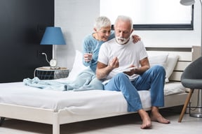 Elderly couple at home, senior grey haired man takes pill while sitting on bed