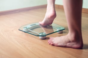Female feet standing on a wooden floor are about to step onto a scale to get a weight measurement