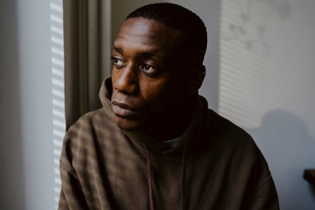 Man with a sad expression looking out a window in a dimly lit room
