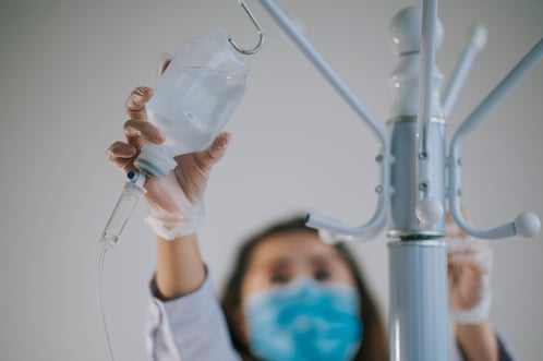 Медицинский работник снимает флакон для внутривенной капельницы с подставки