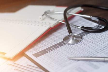 Stethoscope sitting on top of insurance paperwork with health care costs