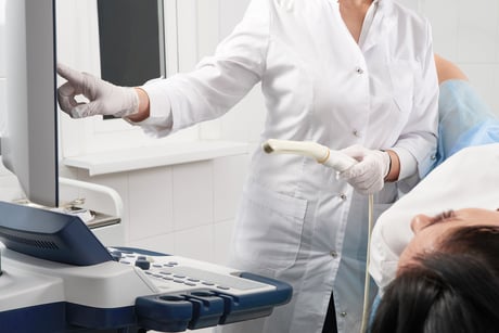 Gynecologist holding transvaginal ultrasound wand after examining a woman and showing results on a screen