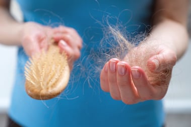 Женщина держит в руках деревянный гребень, очищая его от выпавших волос после расчесывания - побочного эффекта химиотерапии и облучения при раке.