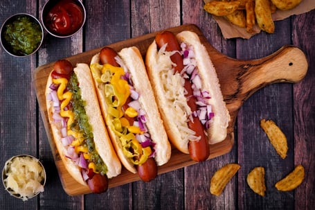 Hot dogs fully loaded with assorted toppings on a paddle board