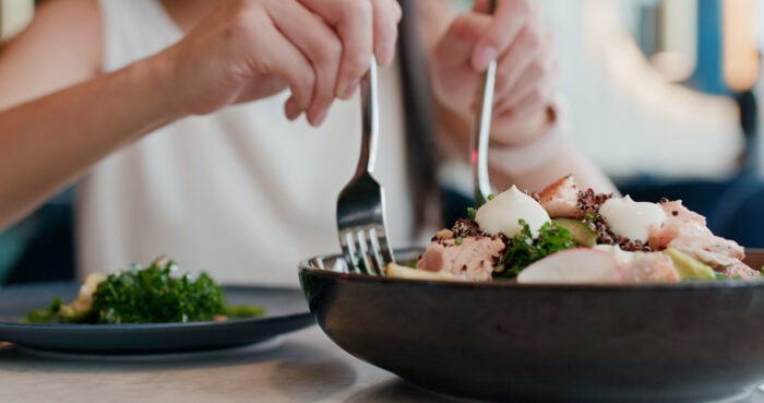 Una foto en primer plano de alguien repartiendo una ensalada de aspecto saludable en un plato separado utilizando dos tenedores.
