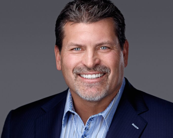 A man in a blue collared button-down and blazer smiles for the camera.