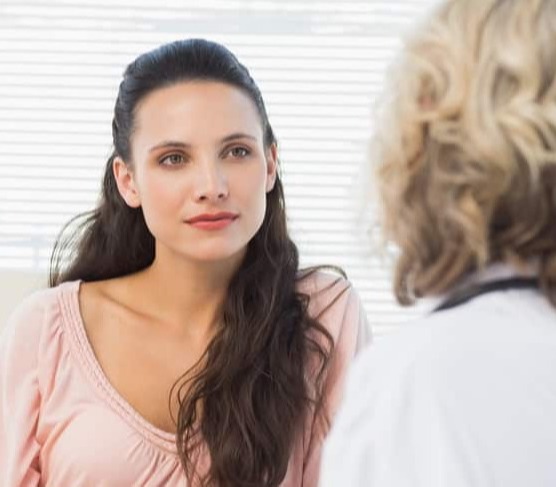 Una mujer de pelo oscuro mira atentamente a su médico, que está de espaldas a la cámara.