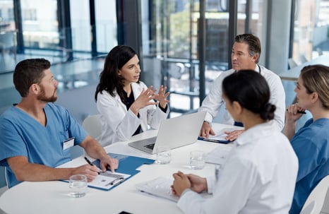 A group of five health care providers have a conversation while sitting around a conference table
