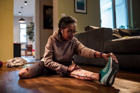 A woman wearing white earphones does a leg stretch