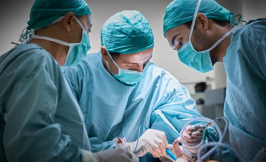 Three men in surgical masks and scrubs performing an operation