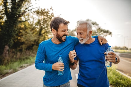 On a tree-lined street, a father and son share a laugh while holding water bottles. 