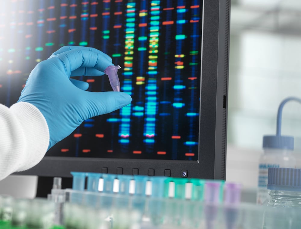 Gloved hand holding test tube up to a screen with biomarkers.