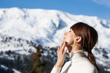 Woman applies sunscreen outside with mountains in background