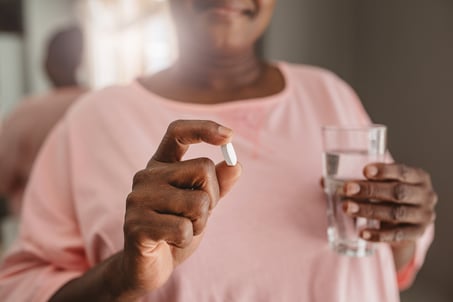 A woman holds a glass of water and a large, white pill