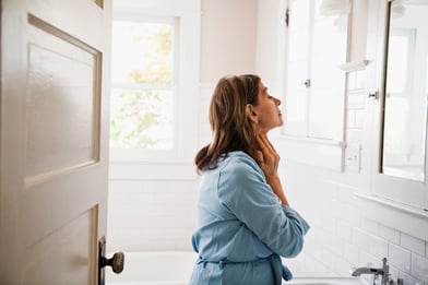 Mujer mirándose en el espejo del baño, tocándose el cuello