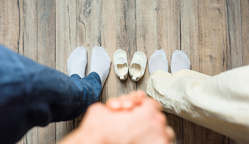 two adults holding hands with a small child's shoes between them