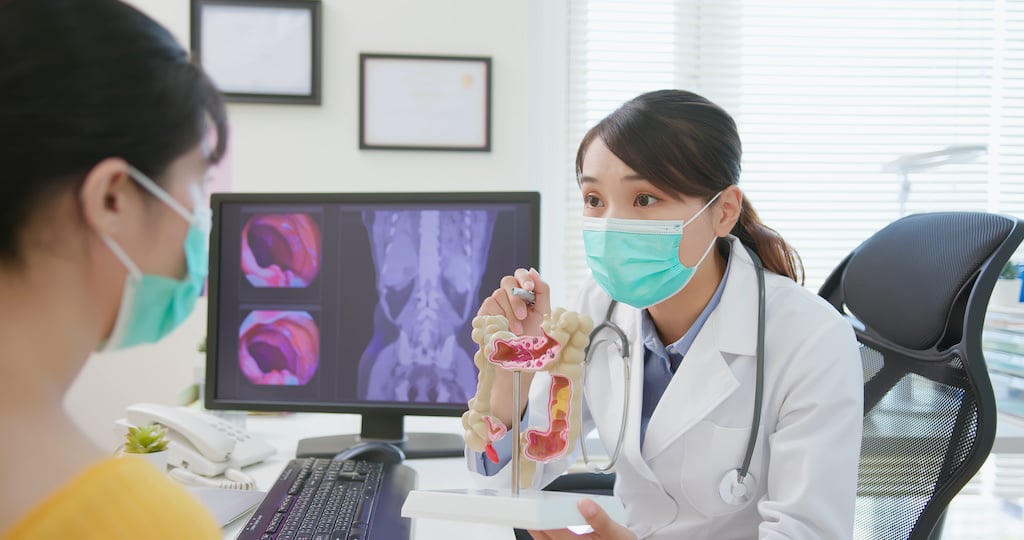 A doctor speaks to a patient with a physical model of a colon.