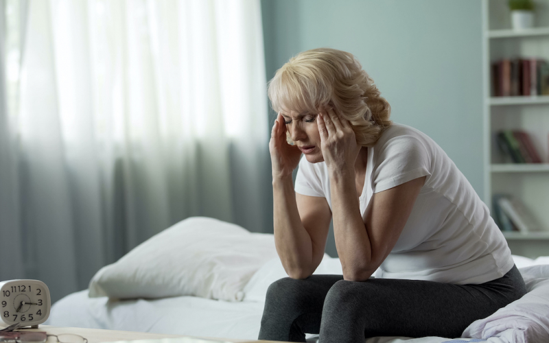 mujer sentada en su cama con dolor de cabeza