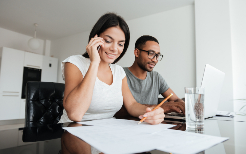 woman talking on phone while man next to her is working on laptop