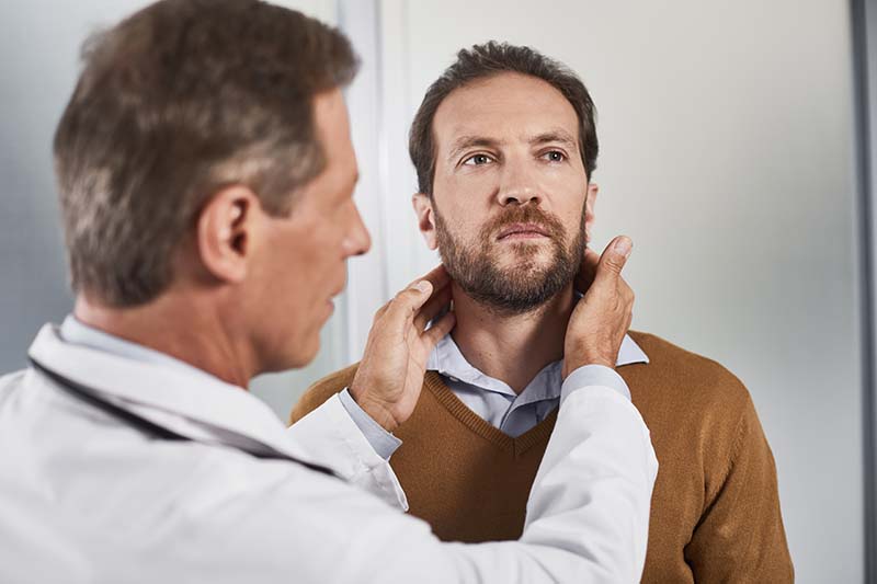 A doctor checks a man for lymphoma symptoms by checking the area under his jaw with his hands.