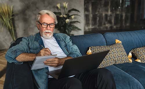man writing on a notepad and on his computer